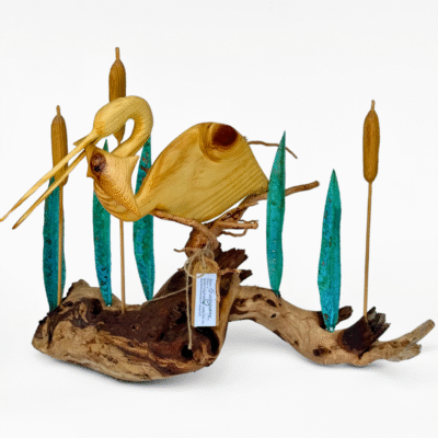 Artisan wooden sculpture of a wading bird on driftwood, featuring striking teal metal reeds and golden wooden cattails, capturing natural marsh beauty.