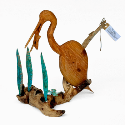 Detailed wooden heron sculpture on a natural driftwood base with verdigris copper reeds and a metal dragonfly. Rustic nature art piece.