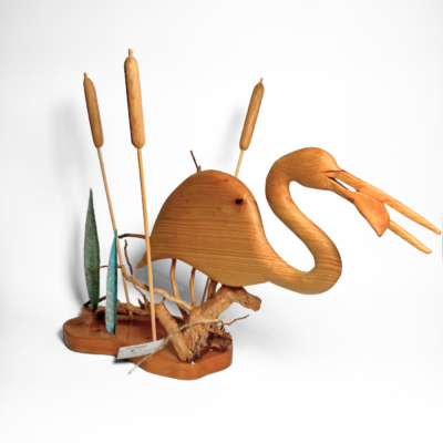 Artisan wooden sculpture of a wading bird on driftwood, featuring striking teal metal reeds and golden wooden cattails, capturing natural marsh beauty.